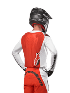 Motocross-rytter iført 2024 Supertech Ward Jersey i farven White Hot Orange, set bagfra, viser det orange rygpanel og de hvide ærmer med sort Alpinestars-branding, kombineret med matchende bukser og sort hjelm, professionelt udstyr til off-road racing