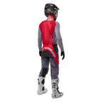 Alpinestars 2024 Supertech Dade trøje, motocross-trøje, Iron Red Berry og grå, set bagfra på en kører, med et rødt rygpanel med gråt logo og grå ærmer, båret med matchende grå og røde racerbukser, hvide støvler og en sort hjelm, professionelt terrænkørselsudstyr