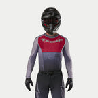 Motocross-kører iført Alpinestars 2024 Supertech Dade-trøje i Iron Red Berry, med rødt brystpanel og grå ærmer med sølvbranding, båret med matchende bukser, sort hjelm og sorte handsker, professionelt off-road racerudstyr
