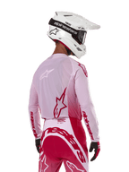 Motocrossrytter set bagfra iført Alpinestars 2024 Supertech Dade Jersey i Red Berry Lilac, med åndbare mesh-paneler og røde Alpinestars-logoer, kombineret med matchende røde og lilla bukser og en hvid Alpinestars-hjelm med goggles, professionelt off-road racerudstyr