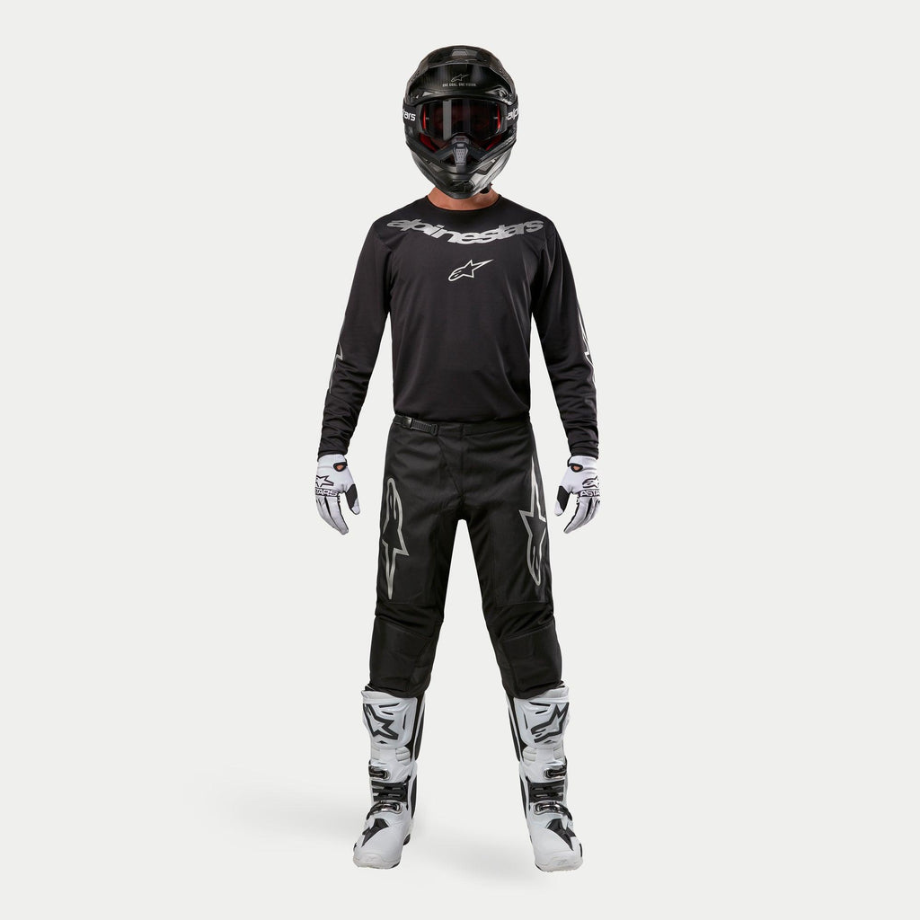 Motocross rider wearing complete racing gear, Alpinestars 2024 Fluid Graphite Jersey in Black Silver, black pants with silver star logos, black helmet with red goggles, white and black boots, white and black gloves, coordinated motocross outfit