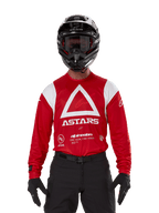 Motocross-kører iført Alpinestars Techdura trøje, stærk rød med hvid grafik, med en stor hvid trekant og ASTARS-logo på brystet, kombineret med en sort hjelm, sorte briller og sort køreudstyr, koordineret sæt til enduro og off-road kørsel