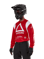 Alpinestars Techdura Jersey, motocross-trøje, klar rød og hvid, med et markant hvidt trekantsdesign og ASTARS-branding, båret med en sort hjelm og handsker, holdbart og fugttransporterende off-road racingudstyr