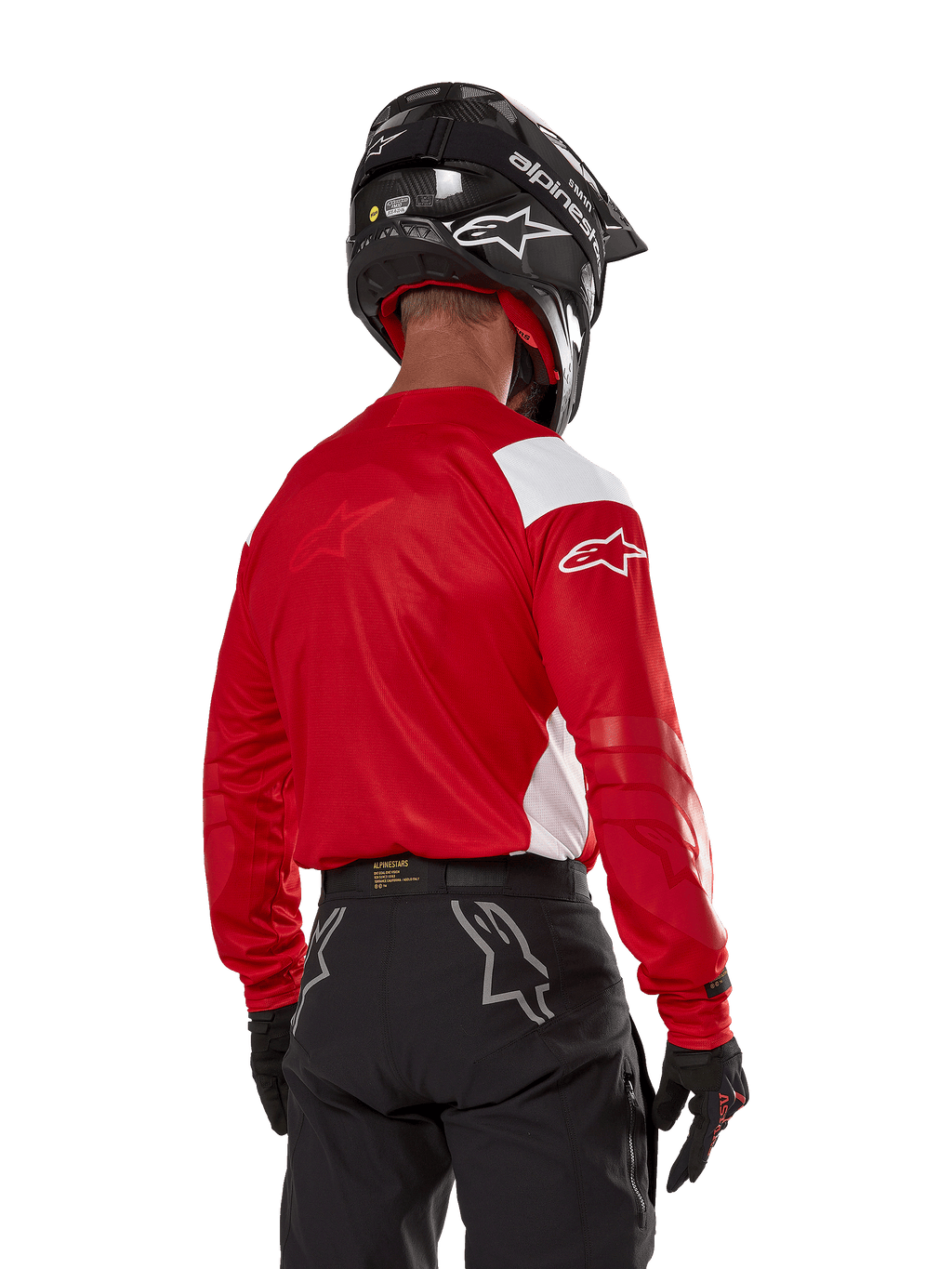 Motocross-kører set bagfra iført Alpinestars Techdura Jersey i Bright Red med hvide paneler, kombineret med sorte off-road bukser, sort hjelm og sorte handsker, koordineret udstyr til enduro- og motocross-kørsel.
