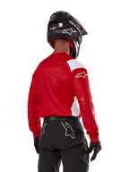 Motocross-kører set bagfra iført Alpinestars Techdura Jersey i Bright Red med hvide paneler, kombineret med sorte off-road bukser, sort hjelm og sorte handsker, koordineret udstyr til enduro- og motocross-kørsel.