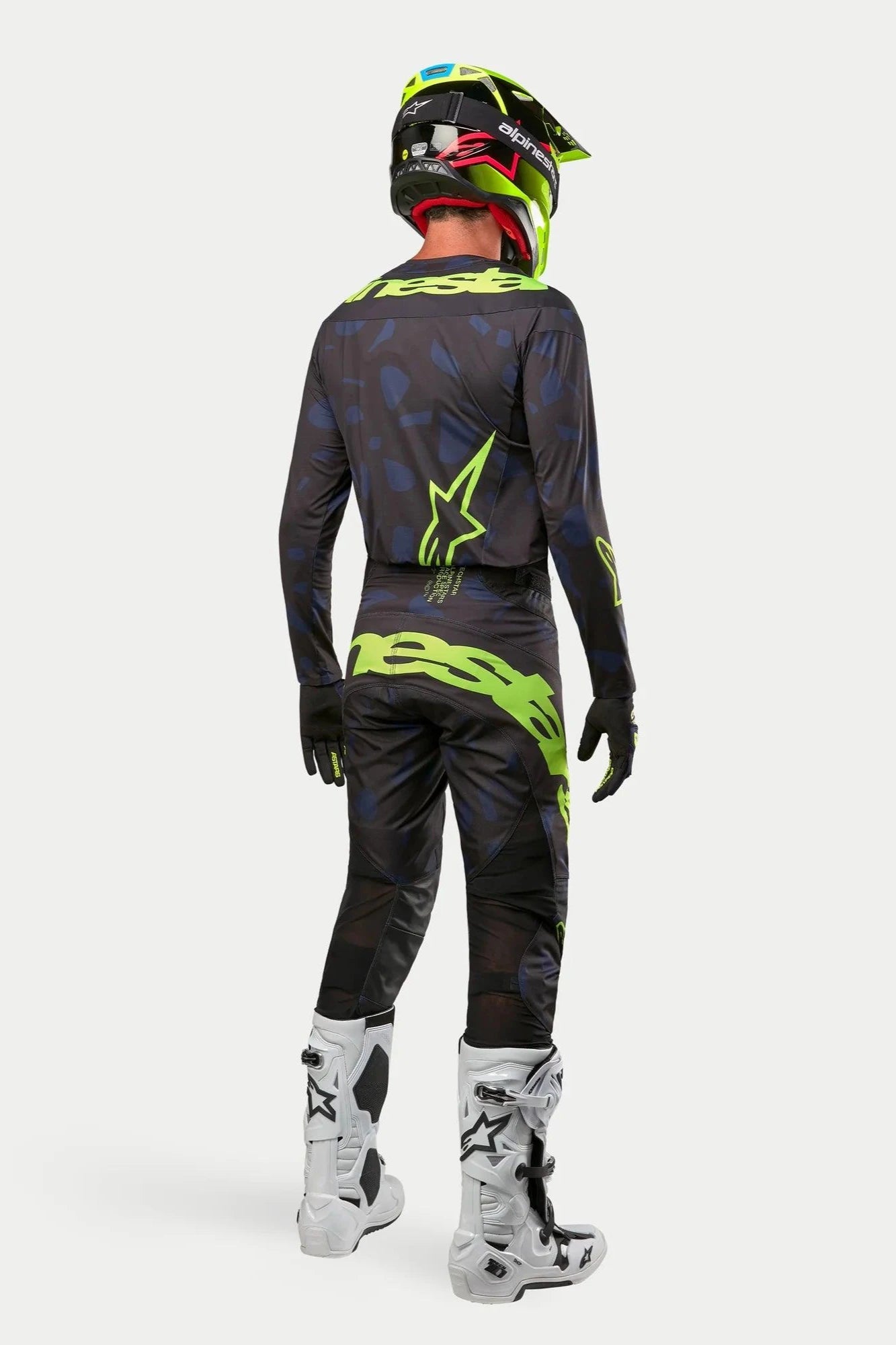 Alpinestars 2024 Techstar Rantera-trøje og -bukser, motocross-kører i fuldt udstyr set bagfra, sort, navyblå og neongul, matchende neongul hjelm og hvide støvler, koordineret off-road racersæt