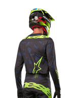 Set bagfra af en motocross-rytter iført Alpinestars 2024 Techstar Rantera Jersey i Black Navy Yellow Fluo, med fremtrædende gul fluo-branding og logoer på ryggen, kombineret med matchende motocross-bukser og en neongul hjelm for et komplet off-road racing-look.