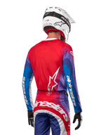 Motocrosskører set bagfra iført Alpinestars 2024 Techstar Pneuma trøje i Blue Mars Red White, med rød ryg og hvidt stjernelogo, blå og lilla ærmer med hvidt branding, koordineret med matchende bukser og en hvid hjelm til terrænkørsel.