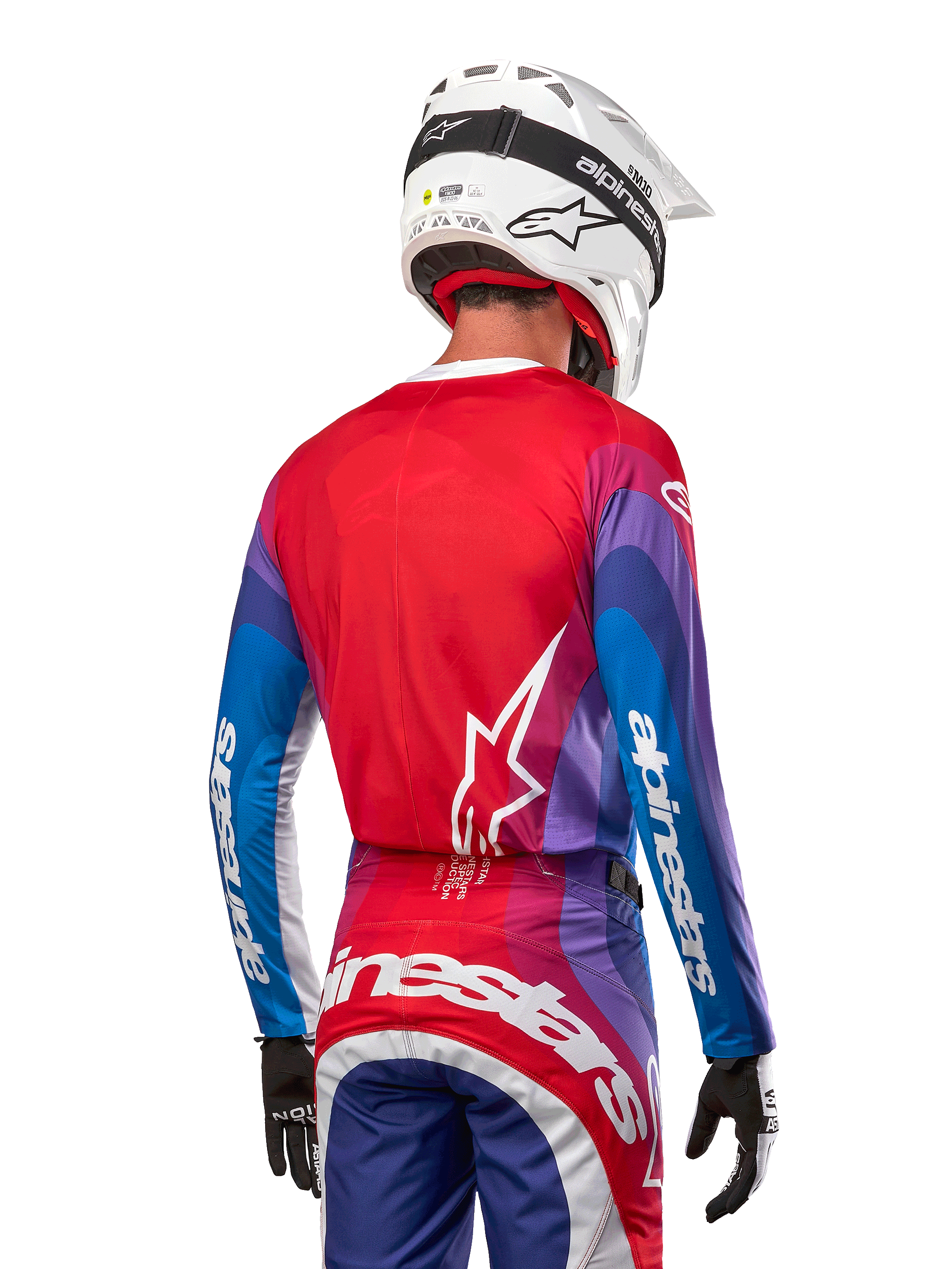Motocrosskører set bagfra iført Alpinestars 2024 Techstar Pneuma trøje i Blue Mars Red White, med rød ryg og hvidt stjernelogo, blå og lilla ærmer med hvidt branding, koordineret med matchende bukser og en hvid hjelm til terrænkørsel.