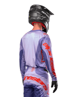 Alpinestars 2024 Techstar Ocuri Jersey, motocross-trøje, lilla og stærk orange, set bagfra på en kører iført matchende udstyr og sort hjelm, med store orange Alpinestars-bogstaver på ærmerne og den nederste del af ryggen