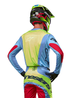 Motocross rider from behind wearing the Alpinestars 2024 Techstar Ocuri Jersey, Light Blue with Fluo Yellow back and Red sleeve accents, matching motocross pants and neon yellow helmet, coordinated outfit for off-road racing