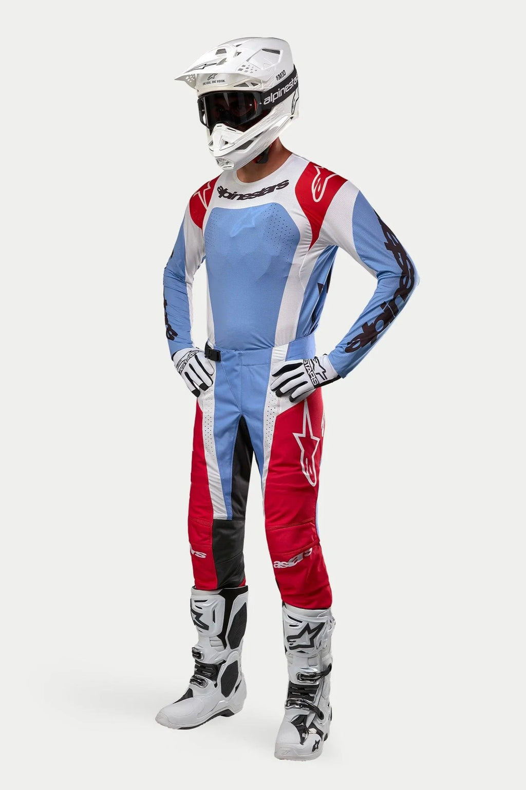 Motocross-kører iført Alpinestars 2024 Techstar Ocuri-udstyr, lyseblå, Mars-rød og hvid trøje og bukser, hvid hjelm med goggles, hvide og sorte handsker og støvler, professionelt raceroutfit til terrænkørsel