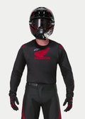 Motocrosskører iført Alpinestars Honda Racer Iconic Jersey i sort og rød, med et stort rødt Honda-vingelogo på brystet og hvidt Astar-logo, kombineret med matchende sort hjelm, briller og handsker for et komplet off-road racersæt