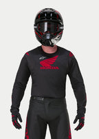 Motocrosskører iført Alpinestars Honda Racer Iconic Jersey i sort og rød, med et stort rødt Honda-vingelogo på brystet og hvidt Astar-logo, kombineret med matchende sort hjelm, briller og handsker for et komplet off-road racersæt