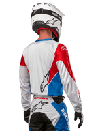 Alpinestars Honda Racer Iconic Jersey, motocross-trøje set bagfra, hvid med klare blå og røde paneler, tydeligt Alpinestars-logo på ryggen, hvid motocrosshjelm og matchende racerbukser, off-road racingudstyr