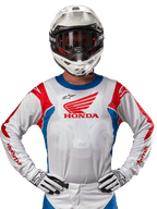 Honda Racer Iconic Jersey, hvid motocross-trøje med rødt Honda-logo og klare blå og røde detaljer, båret af en kører med hvid hjelm og handsker, højtydende udstyr til off-road og motocross-racing
