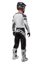 Alpinestars 2024 Racer Hana trøje, motocross-rytter set bagfra, hvid og sort, hvid trøje med sort grafisk branding på ærmerne, kombineret med sorte bukser med hvid Alpinestars-tekst på bagdelen, sort hjelm og hvide og sorte støvler, matchende off-road racing-udstyr