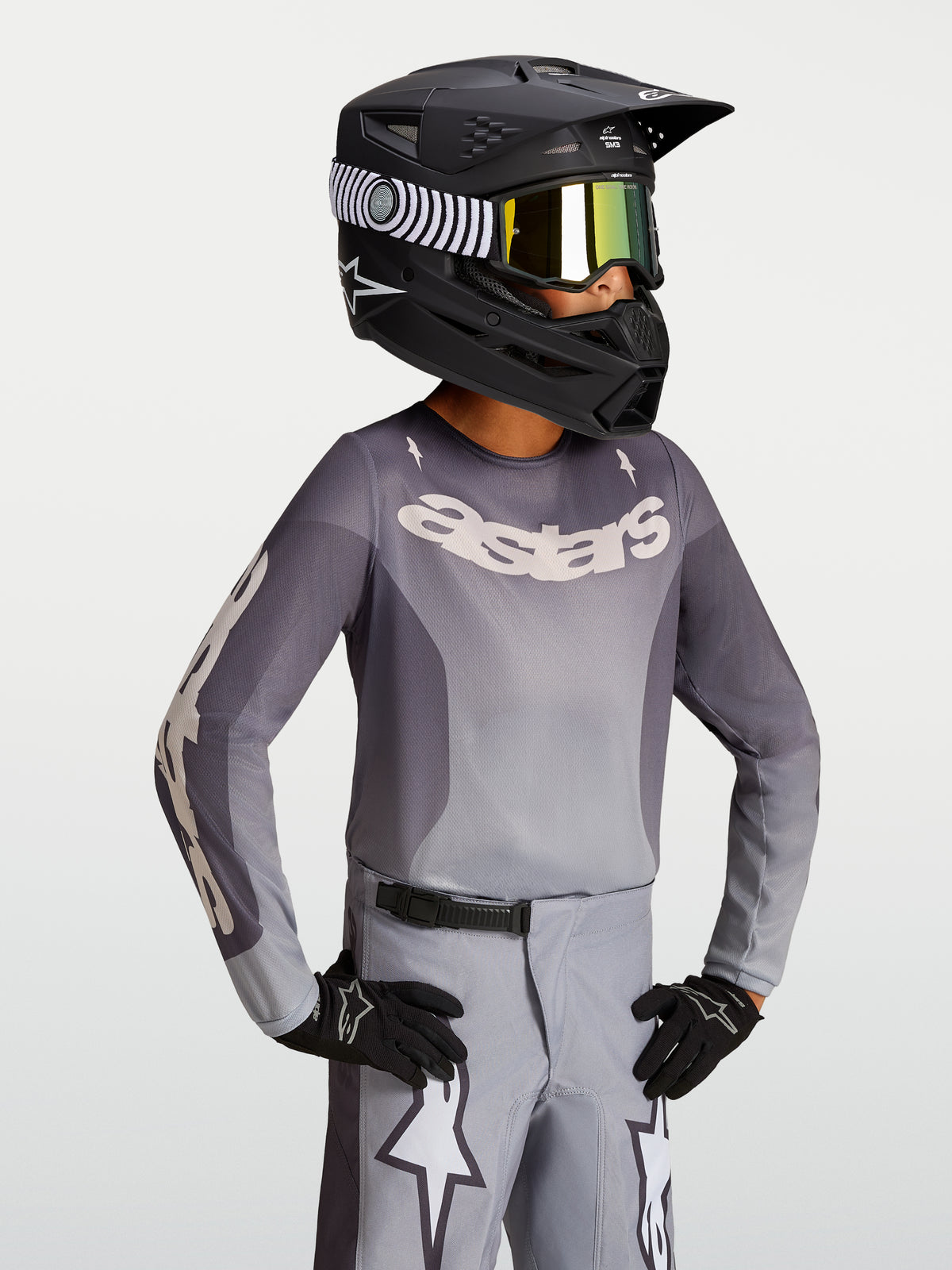 Alpinestars 2027 Youth Fluid Amber Jersey, youth motocross jersey in sand and gray, on-model with a black racing helmet.