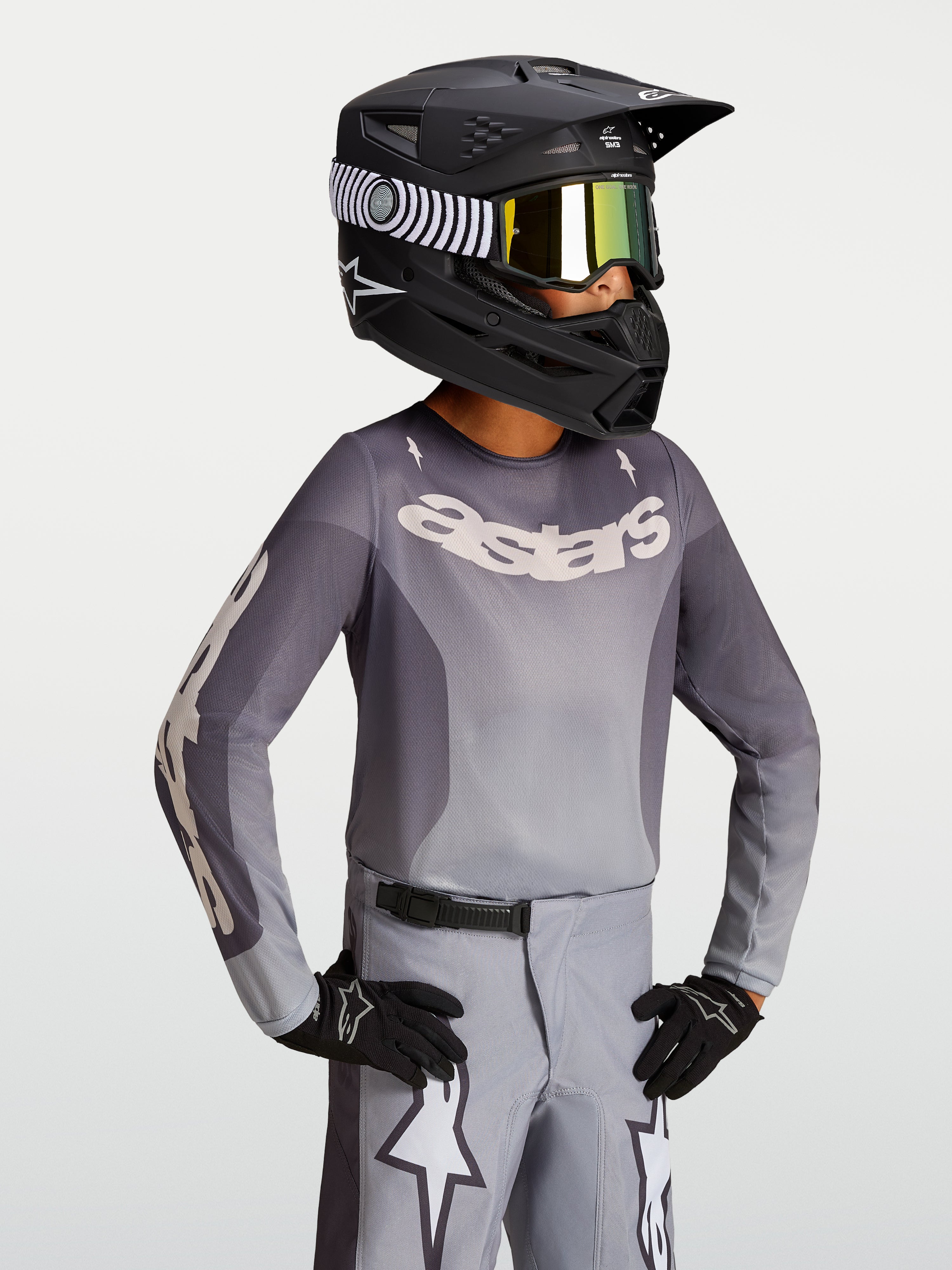 Alpinestars 2027 Youth Fluid Amber Jersey, youth motocross jersey in sand and gray, on-model with a black racing helmet.