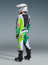 Ung motocross-rytter set bagfra iført Alpinestars 2026 Youth Fluid Portl-jersey, Green White Black-farvevariant med livlige pink detaljer, matchende motocross-bukser, hvid hjelm og sort-hvide støvler, koordineret performance racing-udstyr.