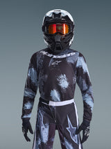 Alpinestars 2026 Youth Fluid Lahnd Jersey, Motocross Jersey, Iron Camo, worn by a youth rider with matching pants, black and white helmet with orange goggles, and black gloves, featuring a splattered grey and black design with white branding, complete off-road racing gear for young riders.