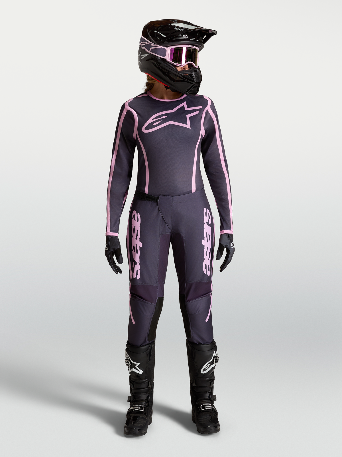 Alpinestars Stella Fluid Apex V2 udstyrssæt til kvinder, grå og pink, motocross-gear vist på model med hjelm og støvler.