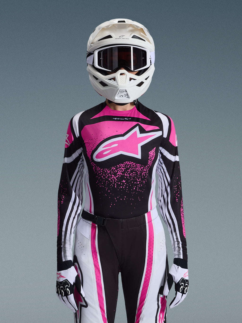 Alpinestars 2026 Stella Techstar Nomur udstyrssæt, motocross-outfit til kvinder, lyserød, sort og hvid med stort stjernelogo, bestående af matchende jersey, bukser og handsker med en hvid hjelm, set forfra på en grå baggrund