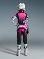 Alpinestars 2026 Stella Techstar Nomur-udstyrssæt, kvindelig motocrosskører set bagfra, lyserød og sort jersey med hvidstribede ærmer og nistret mønster, matchende bukser med hvidt Alpinestars-logo, hvid hjelm og hvide off-road støvler
