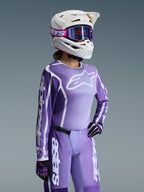 Motocross-kører iført Alpinestars 2026 Woman Stella Fluid Apex Gear Set, lilla og hvid jersey med Alpinestars-logoer, matchende lilla bukser, hvid hjelm med lilla goggles og sort-lilla handsker, professionelt off-road racingudstyr