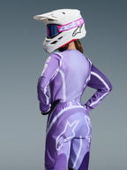 Alpinestars 2026 Stella Fluid Apex-udstyrssæt, motocross-kører iført lilla og lavendelfarvet trøje og bukser med hvid grafik, hvid hjelm med lyserøde og lilla goggles, specifik pasform til kvinder, koordineret udstyr til off-road-kørsel