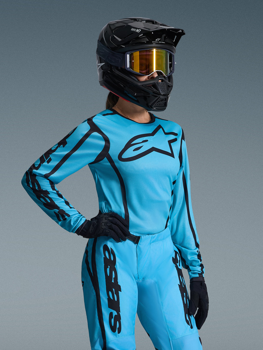 Alpinestars 2026 Stella Fluid Apex udstyrssæt til damer, lyseblå og sort, motocross-trøje og bukser med sort branding, båret med sort hjelm, guld-spejlbriller og sorte handsker, dedikeret damepasform til off-road racing