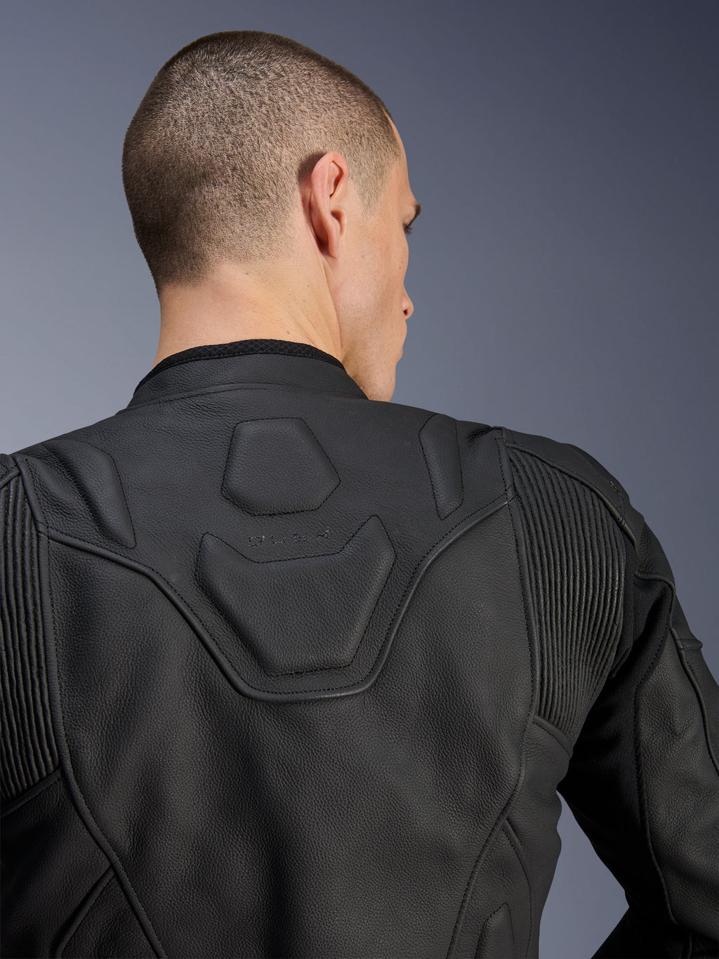 Alpinestars Dusk læderjakke, sort, nærbillede af den øverste del af ryggen og skuldrene, der viser det prægede DUSK-logo på et polstret panel, læder stretch-accordion, førsteklasses konstruktion i bovint læder