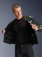 Mandlig model iført Alpinestars T-Sps Air v2-jakke i sort og gul fluo, vist åben for at fremhæve den indvendige mesh-konstruktion og lommer, kombineret med et sort Alpinestars baselayer og sorte bukser, urban motorcykeludstyr-stil