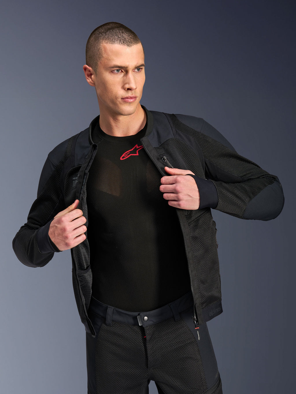Alpinestars Troop-Air Pro jakke, sort, premium teknisk pansret luftjakke med mesh-konstruktion, båret åben over et sort base layer med et rødt logo, kombineret med matchende mesh-motorcykelbukser, urban moderne kørestil