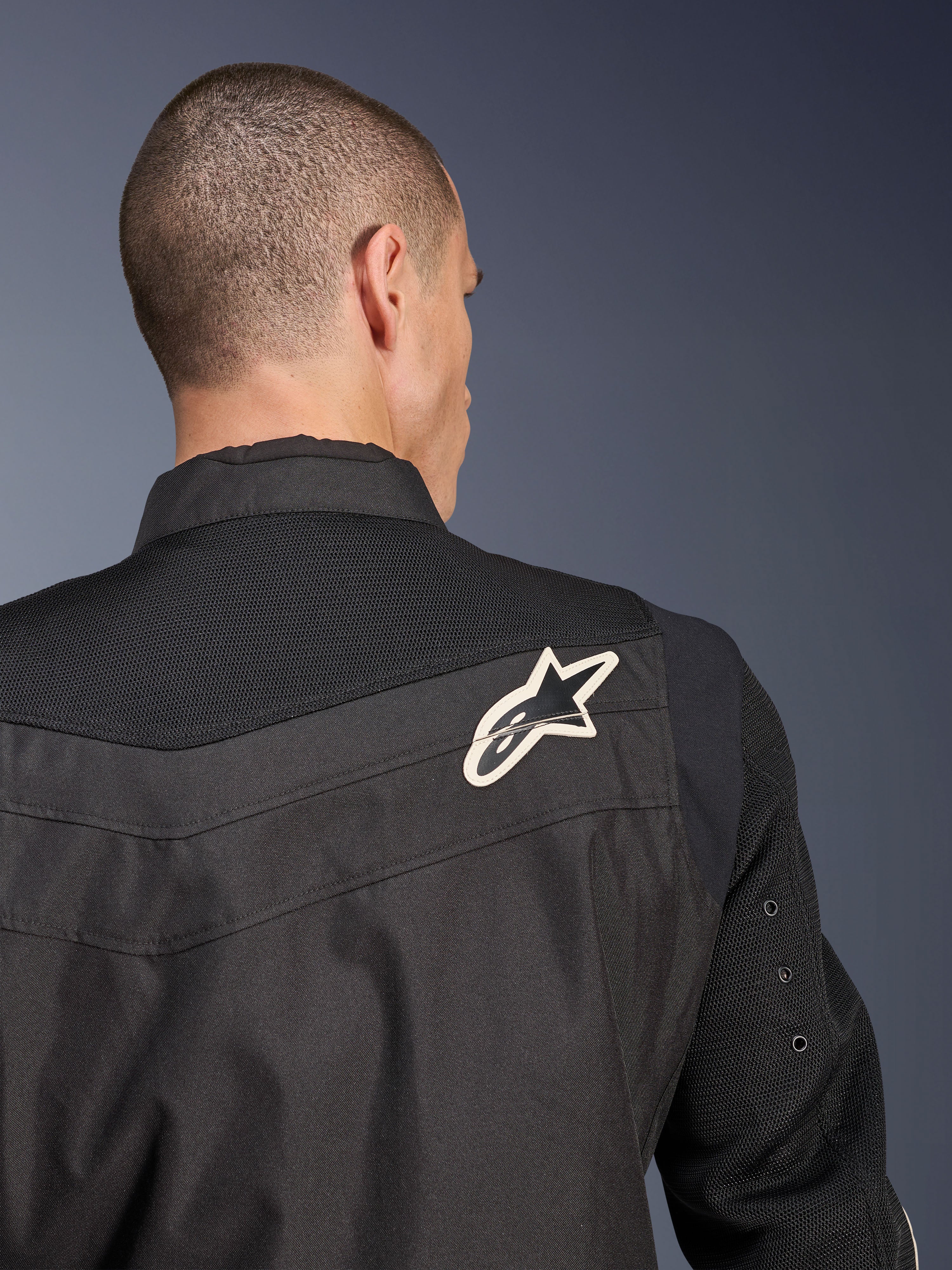 Alpinestars T-Dyno Air Jakke, sort tekstil motorcykeljakke, nærbillede bagfra der fremhæver det åndbare 3D-mesh-bærestykke og ærmerne, hvidt og sort stjernelogo på højre skulder