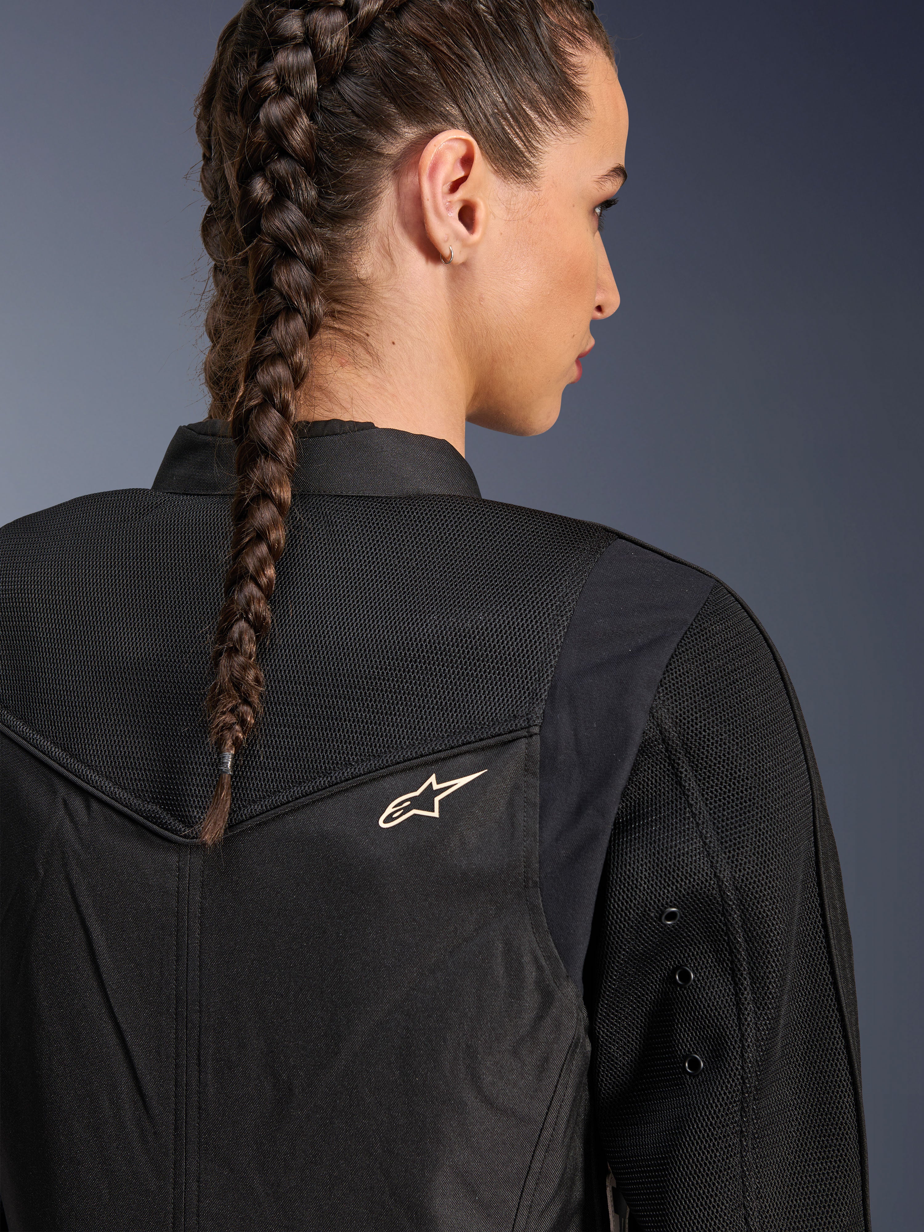 Alpinestars Stella T-Dyno Air Jakke, sort motorcykeljakke til kvinder, nærbillede bagfra der viser 3D-mesh-paneler på bærestykket og den øvre ryg for luftstrøm, med et lille hvidt stjernelogo, båret af en model med flettet hår.