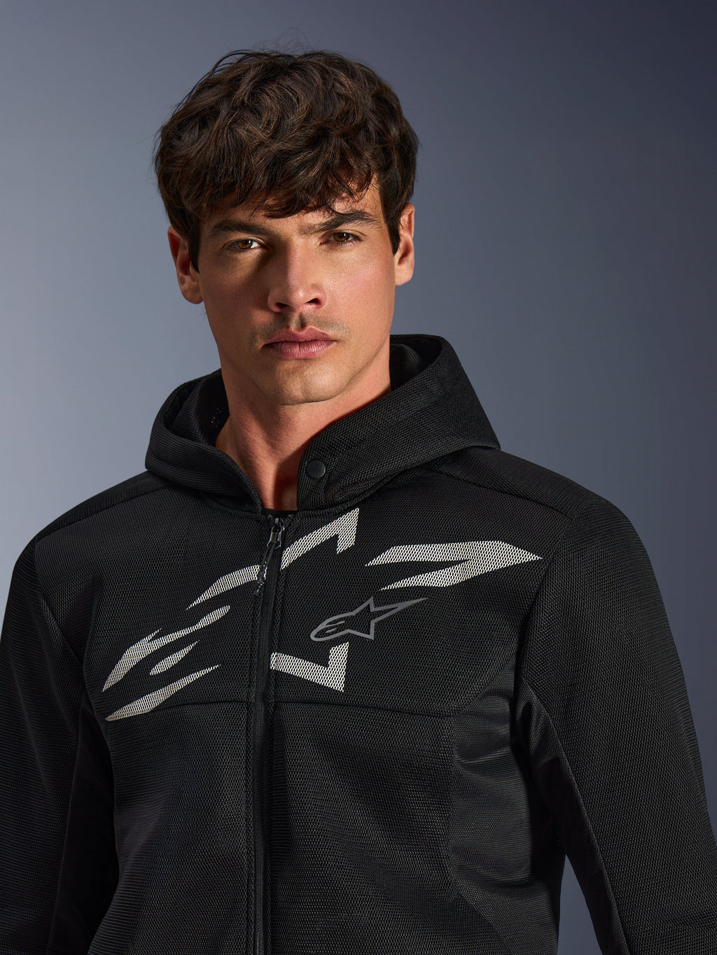 Alpinestars Chrome Superairflow Hoodie, sort motorcykelhættetrøje, har 3D mesh-konstruktion med et stort hvidt grafisk logo på brystet, båret af en model, beklædning til urban sportskørsel med et moderne ventileret design
