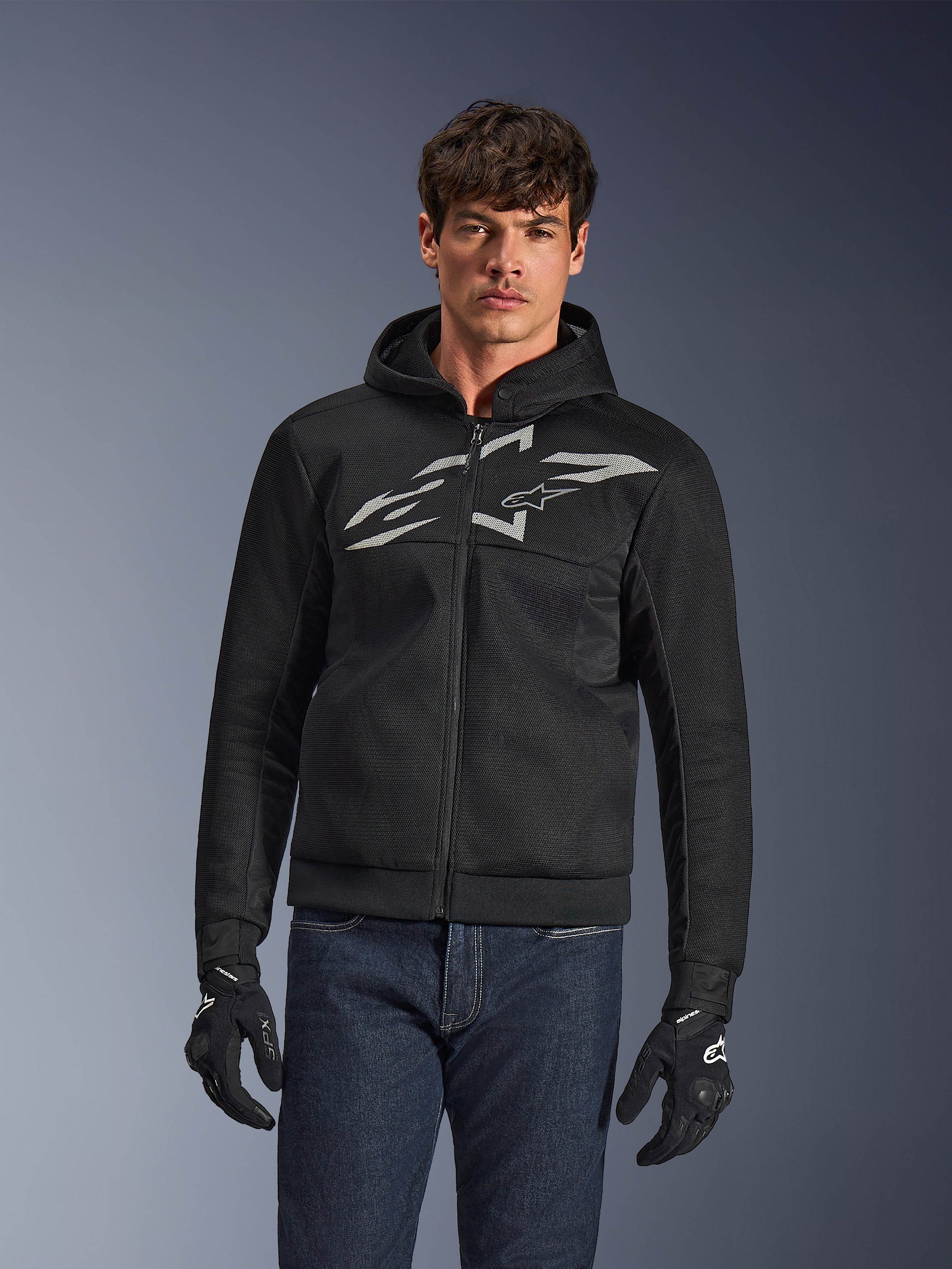 Alpinestars Chrome Superairflow Hoodie, sort motorcykelhættetrøje med lynlås, stort hvidt logo på brystet, mesh-konstruktion for luftgennemstrømning, båret med blå jeans og sorte handsker, sporty urbant køreudstyr