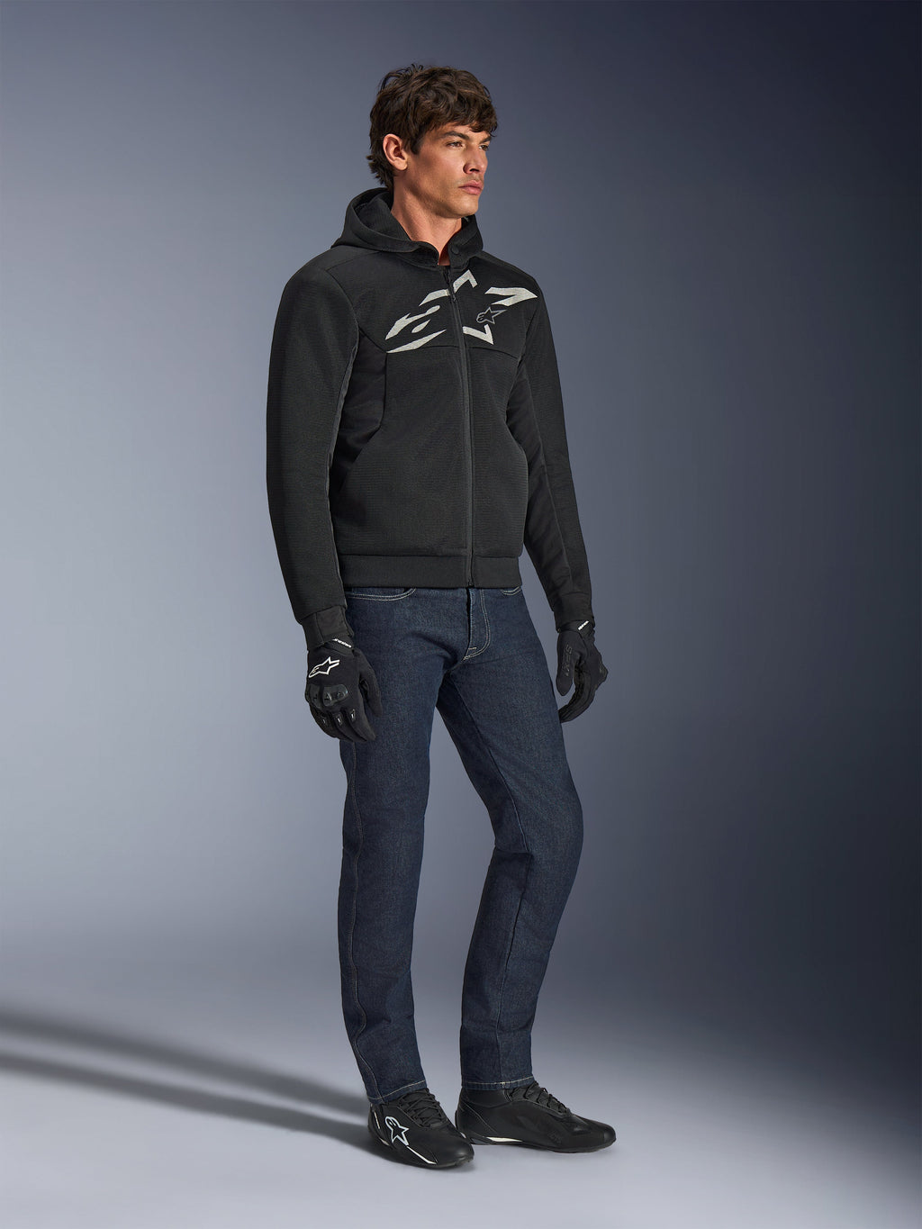 Alpinestars Chrome Superairflow Hoodie, sort med hvidt og gråt logo, ventileret 3D mesh-tekstilkonstruktion, båret med mørkeblå denimjeans og sorte motorcykelhandsker, urban sport-kørestil.