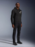 Alpinestars Chrome V2 Sport Hoodie, sort motorcykelhættetrøje med hvidt stjernelogo, båret af en mandlig model med matchende sorte bukser og køre-sneakers, urban lifestyle køreudstyr