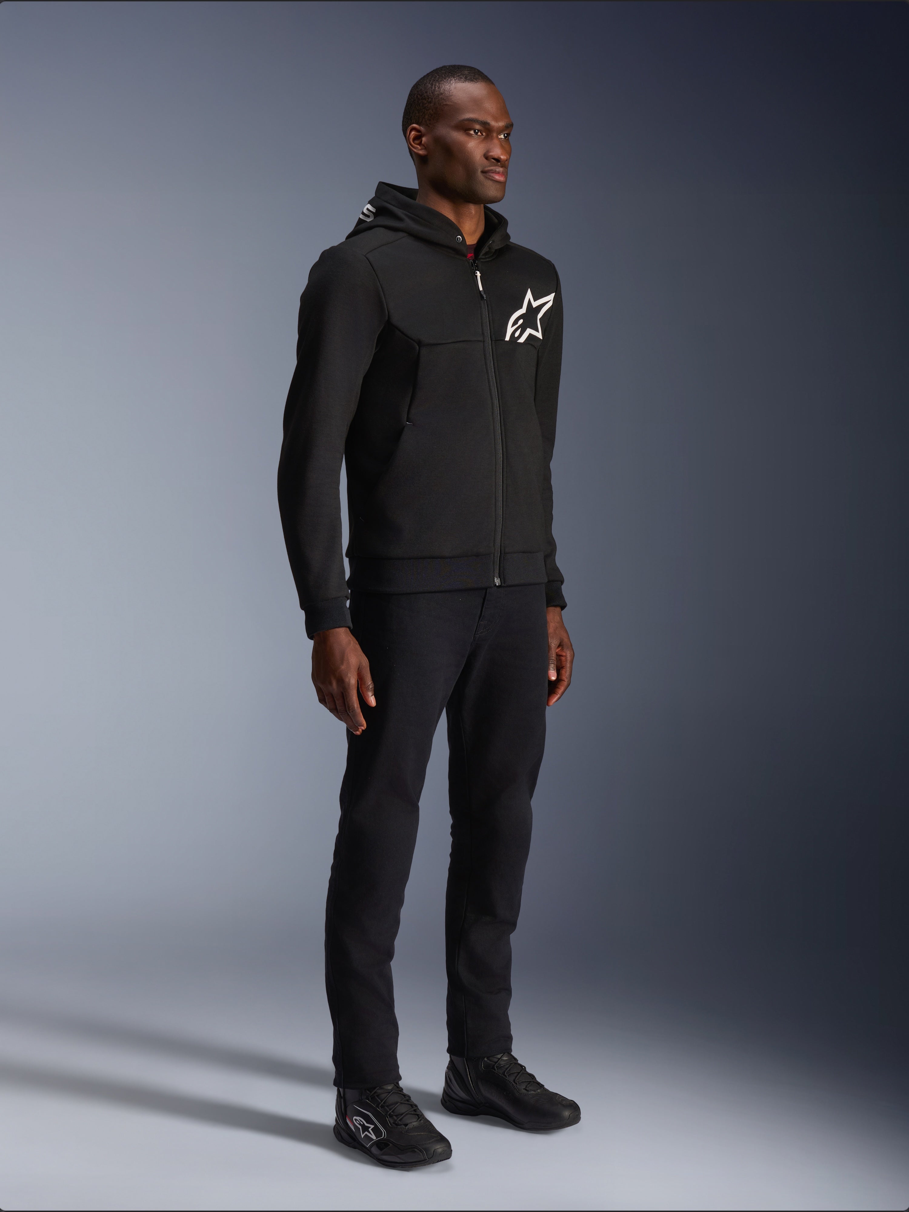 Alpinestars Chrome V2 Sport Hoodie, sort motorcykelhættetrøje med hvidt stjernelogo, båret af en mandlig model med matchende sorte bukser og køre-sneakers, urban lifestyle køreudstyr