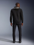 Alpinestars Chrome V2 Sport Hoodie, motorcykel-hættetrøje, sort, model set bagfra iført sort tech fleece-hættetrøje med hvidt Alpinestars-logo på hætten, kombineret med sorte bukser og støvler, afslappet urban kørestil