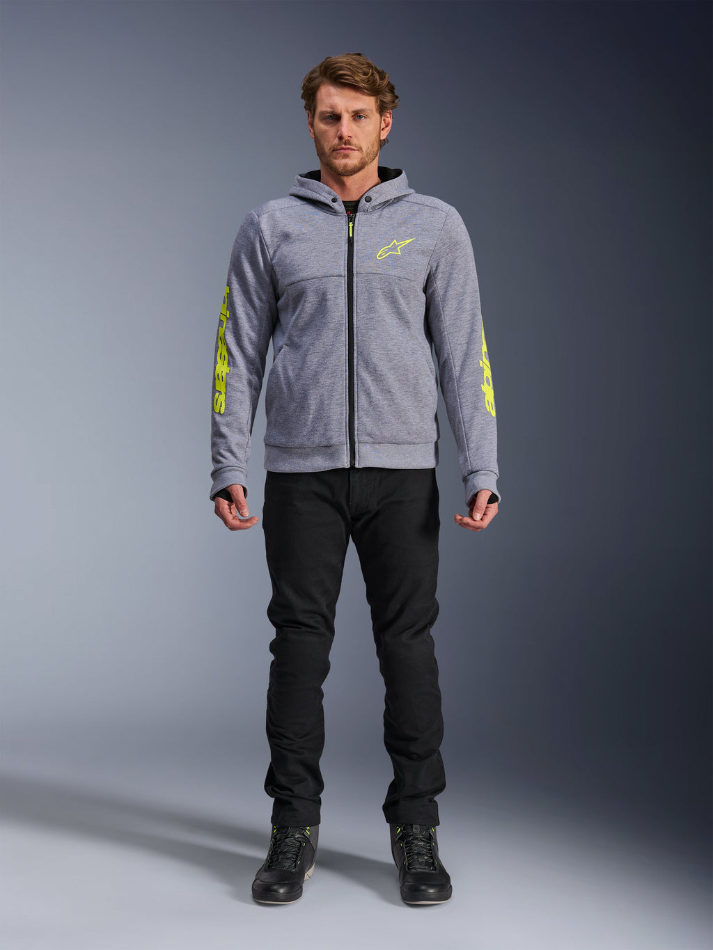 Alpinestars Chrome V2 Sport Hoodie, gråmeleret med fluoriserende gule detaljer, urbant motorcykeltøj, vist med sorte bukser og sorte køresko, teknisk fleece med markant gul branding på ærmer og bryst, afslappet street-stil til kørsel