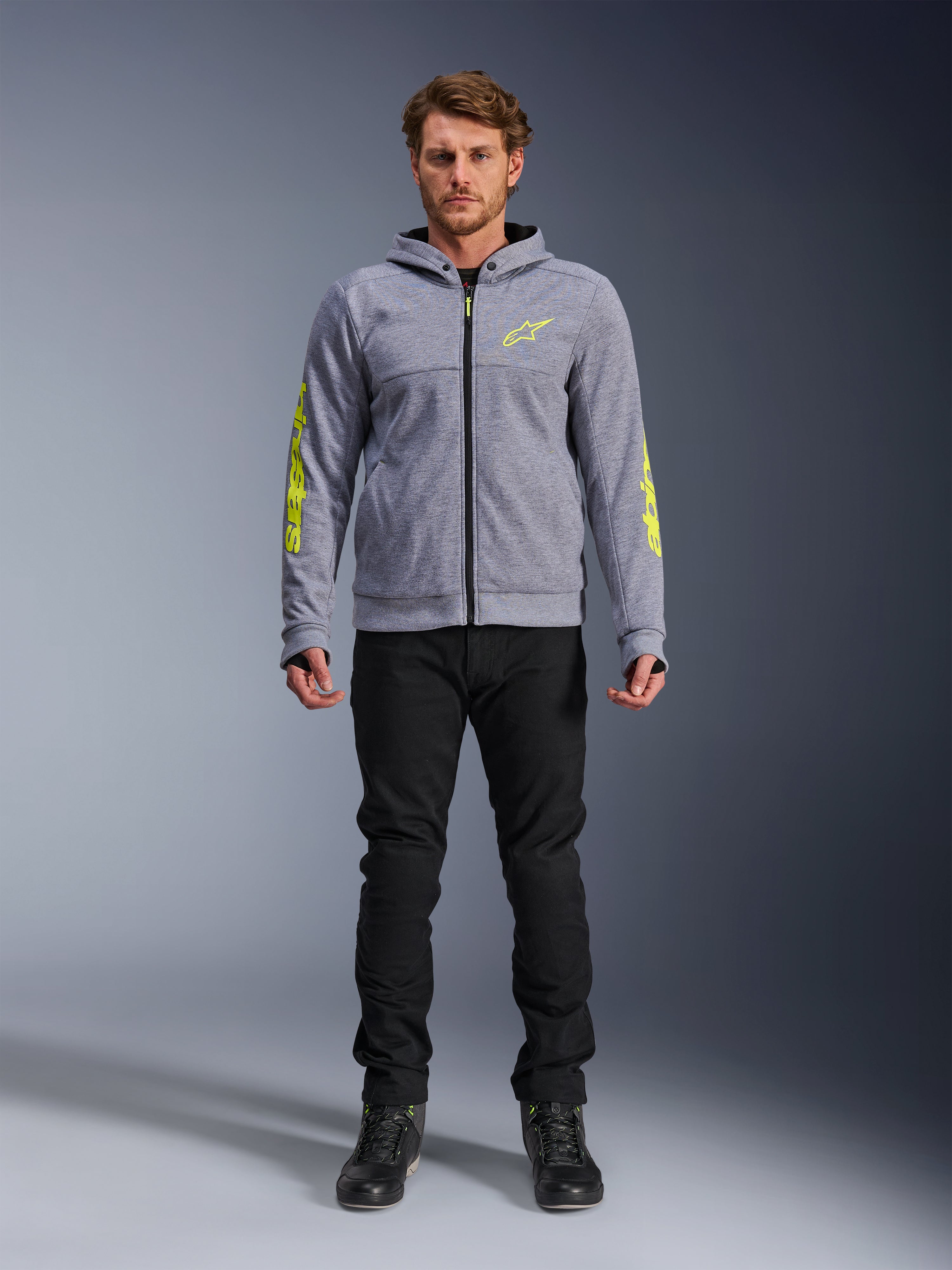 Alpinestars Chrome V2 Sport Hoodie, gråmeleret med fluoriserende gule detaljer, urbant motorcykeltøj, vist med sorte bukser og sorte køresko, teknisk fleece med markant gul branding på ærmer og bryst, afslappet street-stil til kørsel