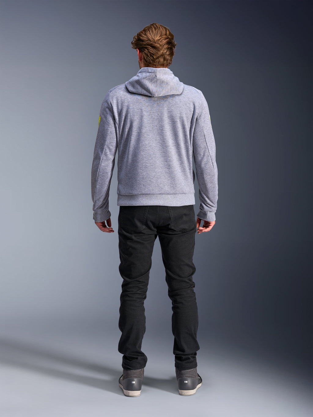 Alpinestars Chrome V2 Sport Hoodie, Gray Heather Fluo Yellow, set bagfra af urbant motorcykeludstyr, tech fleece-hættetrøje båret med sorte bukser, med fluorgule detaljer på ærmerne.