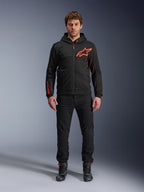 Alpinestars Chrome Air Sport Hoodie, sort og fluorescerende rød, urban motorcykeljakke med tech-fleece-konstruktion, med et stort rødt Astars-logo på brystet og branding på ærmet, båret af en model med sorte bukser og køresko
