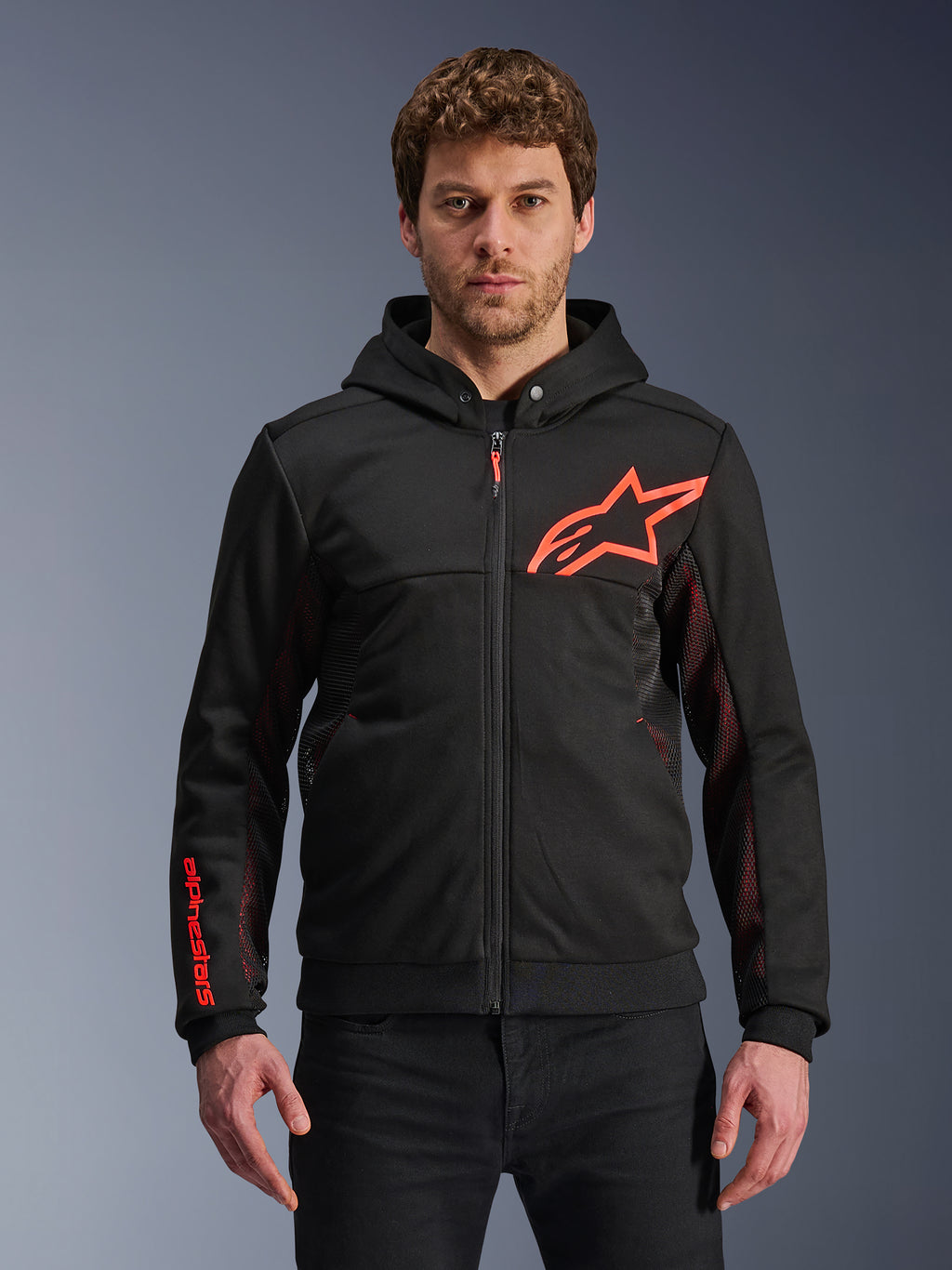 Alpinestars Chrome Air Sport Hoodie, sort hættetrøje med lynlås, rødt fluo stjerne-logo og detaljer på ærmerne, røde mesh-sidepaneler til ventilation, afslappet urban kørebeklædning båret af en model