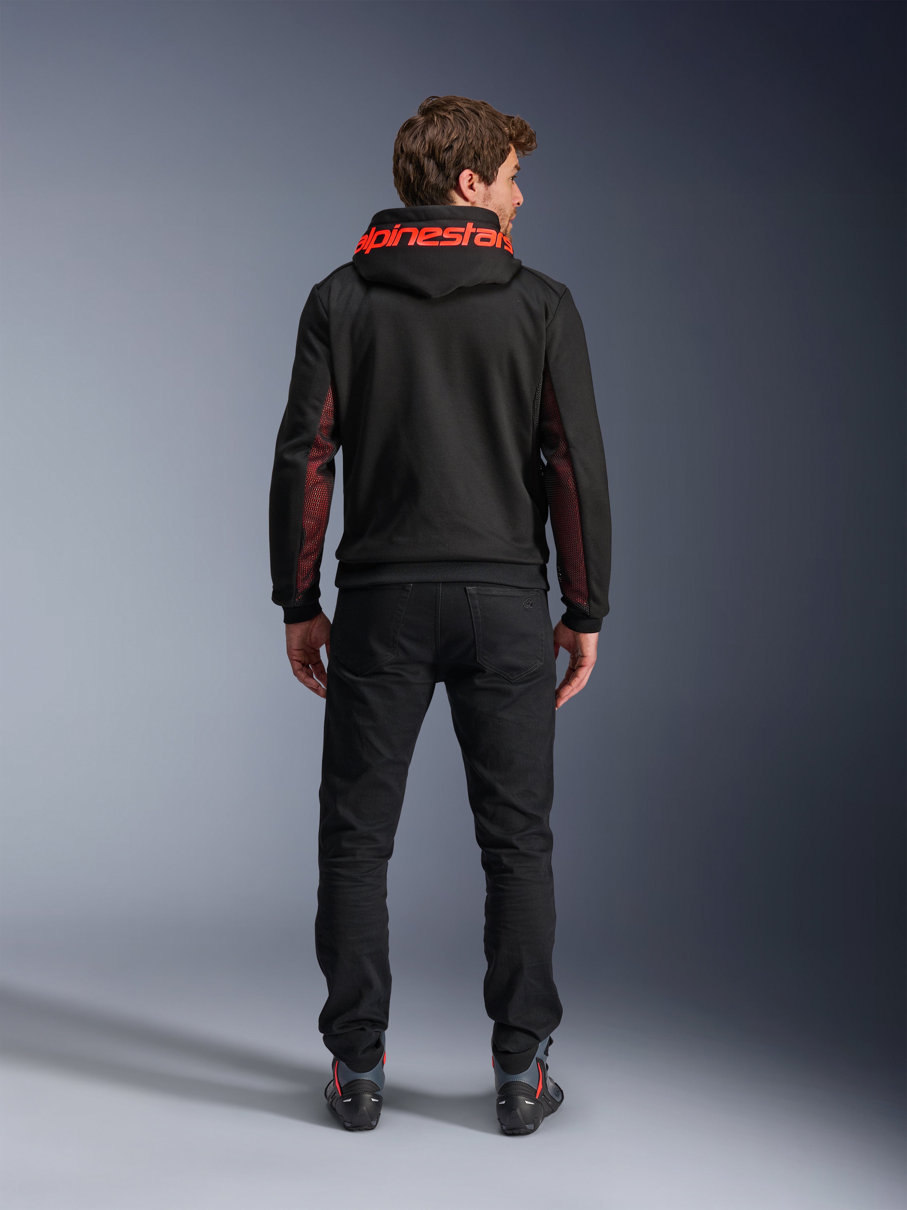 Alpinestars Chrome Air Sport Hoodie, Black and Red Fluo, set bagfra af mand iført afslappet motorcykeljakke, med rød Alpinestars-branding på hætten og røde mesh-paneler på ærmerne, kombineret med sorte bukser