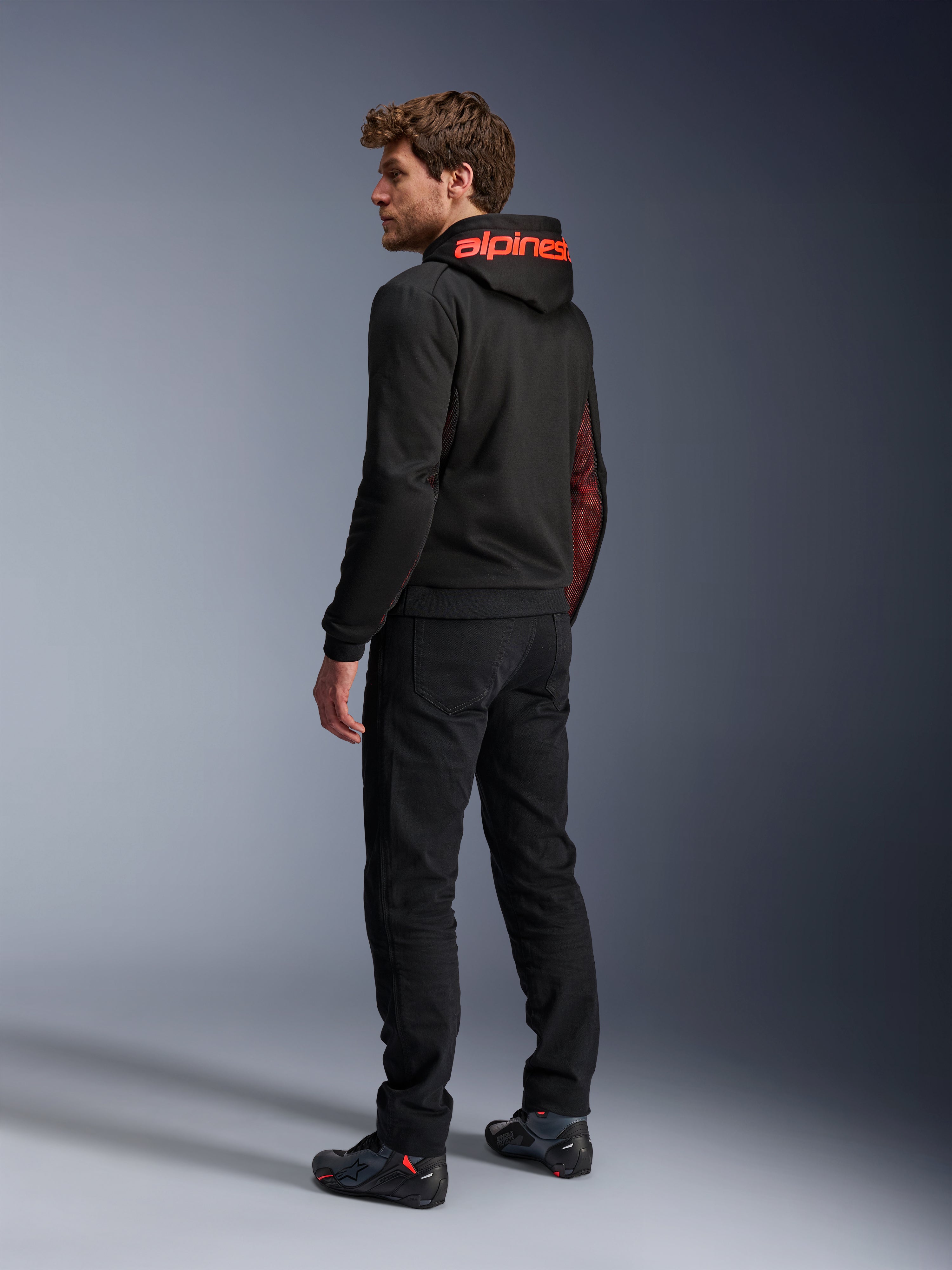 Alpinestars Chrome Air Sport Hoodie, urban motorcykel-hættetrøje, sort og rød fluo, set bagfra med rødt Alpinestars-branding på hætten og mesh-sidepaneler, båret med sorte kørebukser og teknisk fodtøj