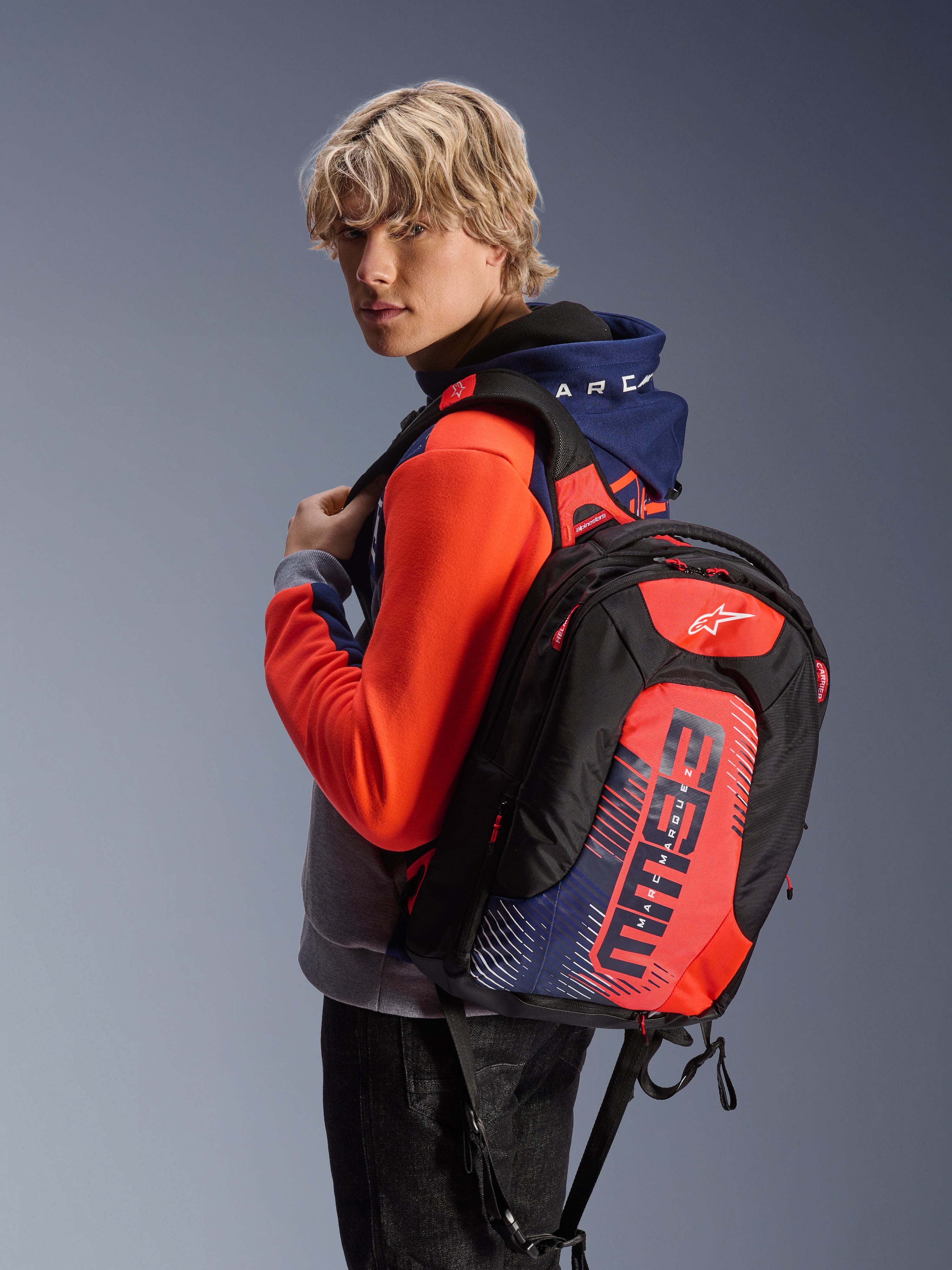 Alpinestars MM93 City Hunter V2 rygsæk, sort med rød fluo og navyblå detaljer, med Marc Marquez MM93 signaturgrafik, båret sammen med en matchende sportshoodie, slank aerodynamisk profil til motorcykelpendling